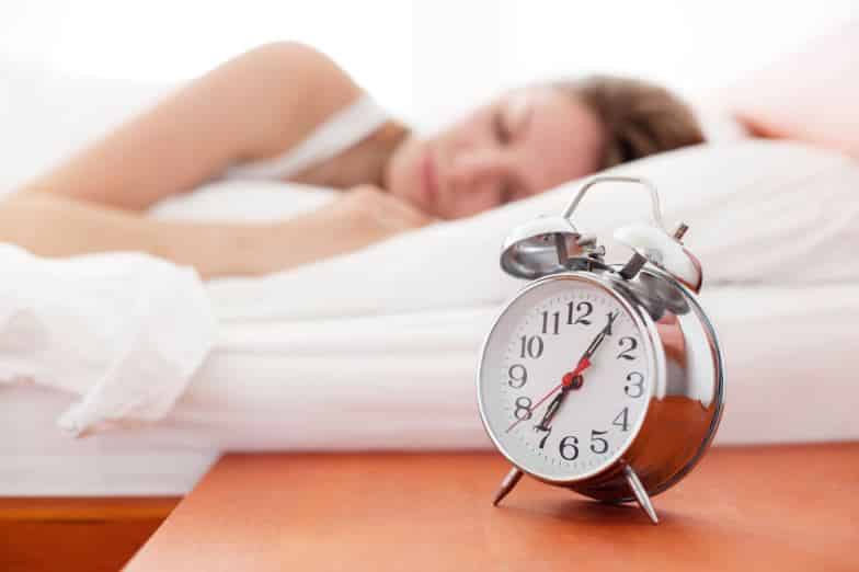 Person sleeping with alarm clock on nightstand